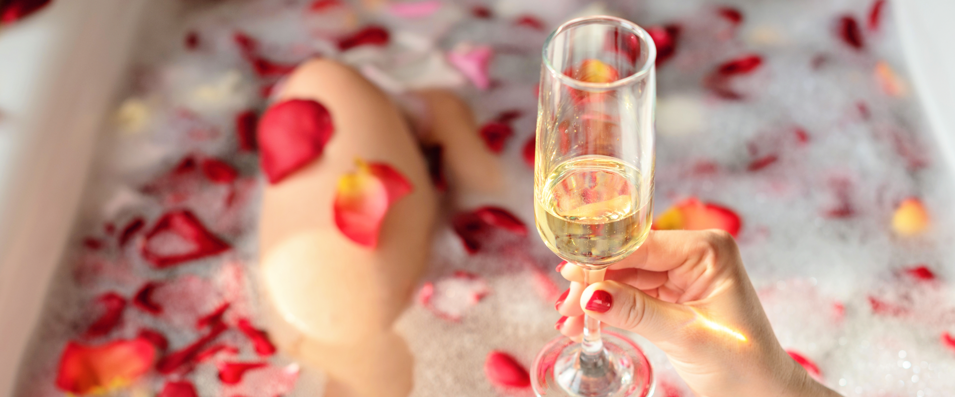 Mulher na banheira com pétalas de rosas e champagne.
