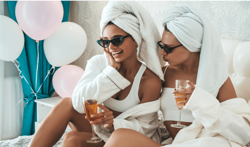 Mulheres sentadas na cama tomando champagne.