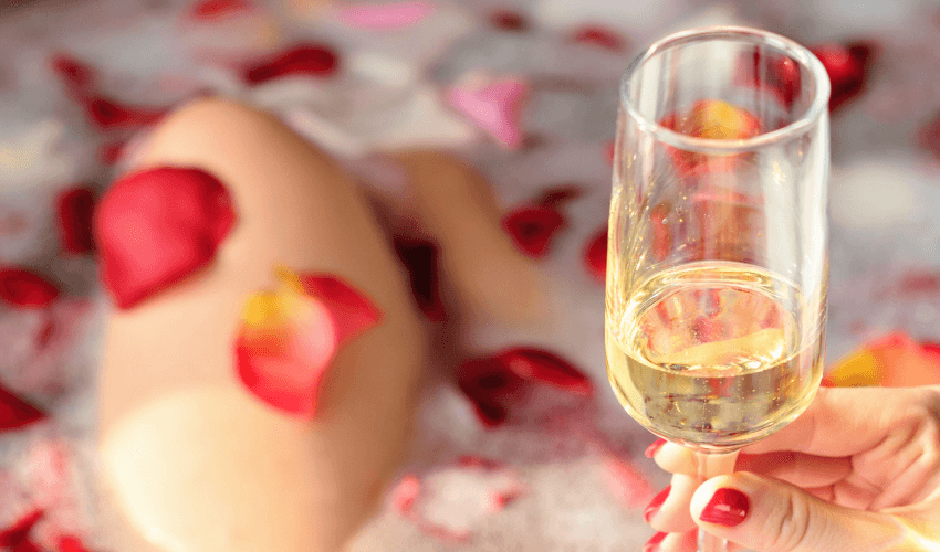 Mulher na banheira com pétalas de rosas e champagne.