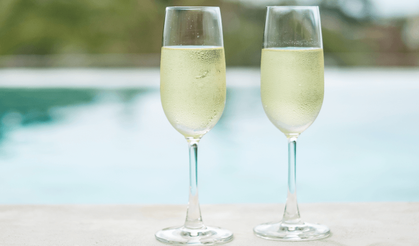 Duas taças com champagne próximas de uma piscina.