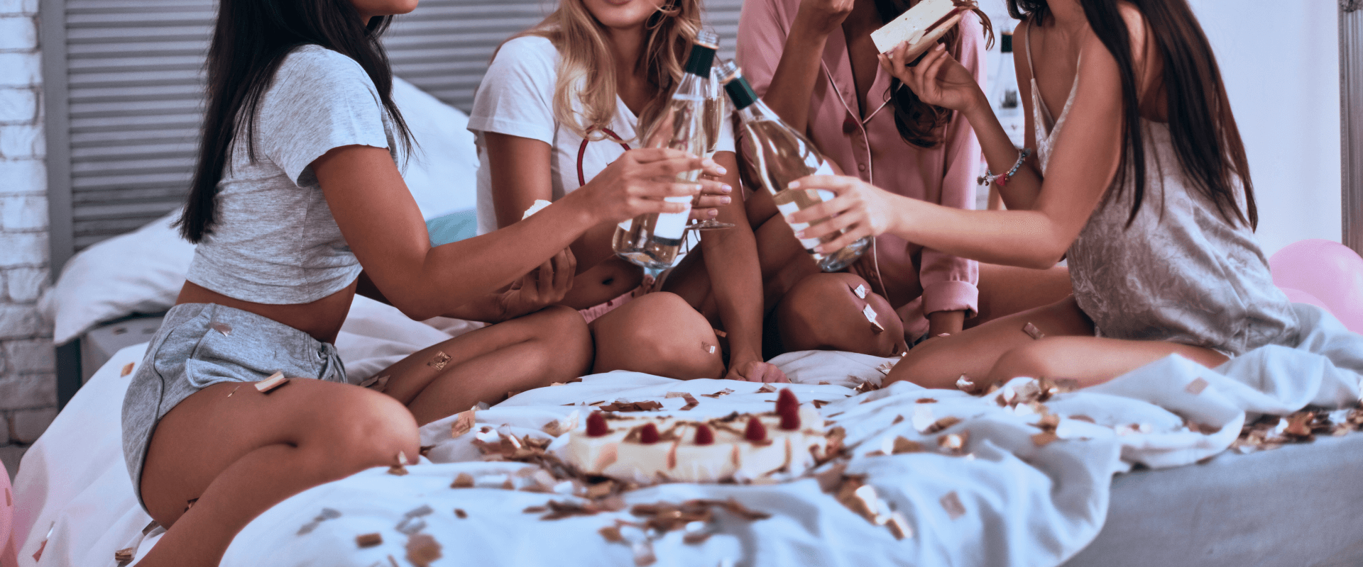 Mulheres sentadas na cama brindando com champagne.
