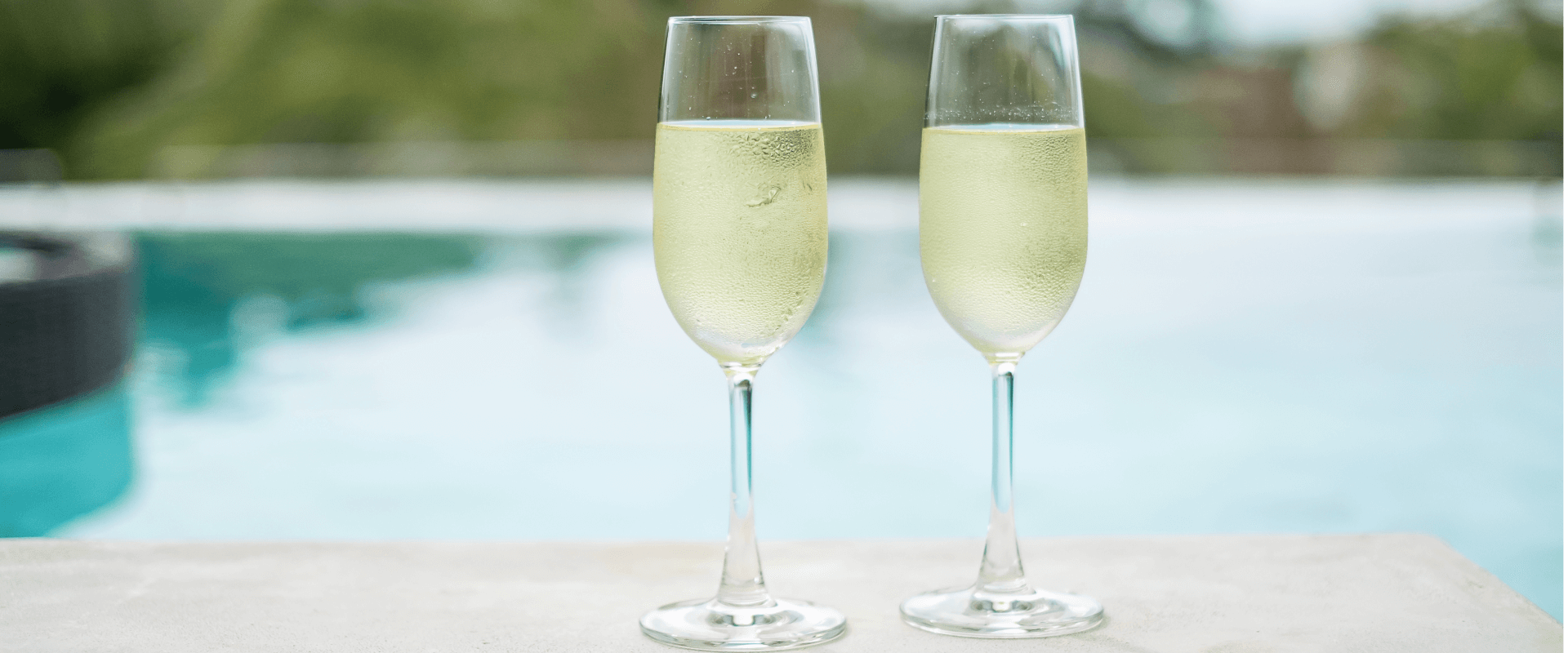 Duas taças com champagne próximas de uma piscina.